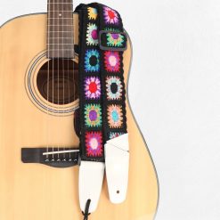 Sangle guitare bohème Crochet Flower à carrés de fleurs au crochet sur fond noir, posée sur une guitare acoustique