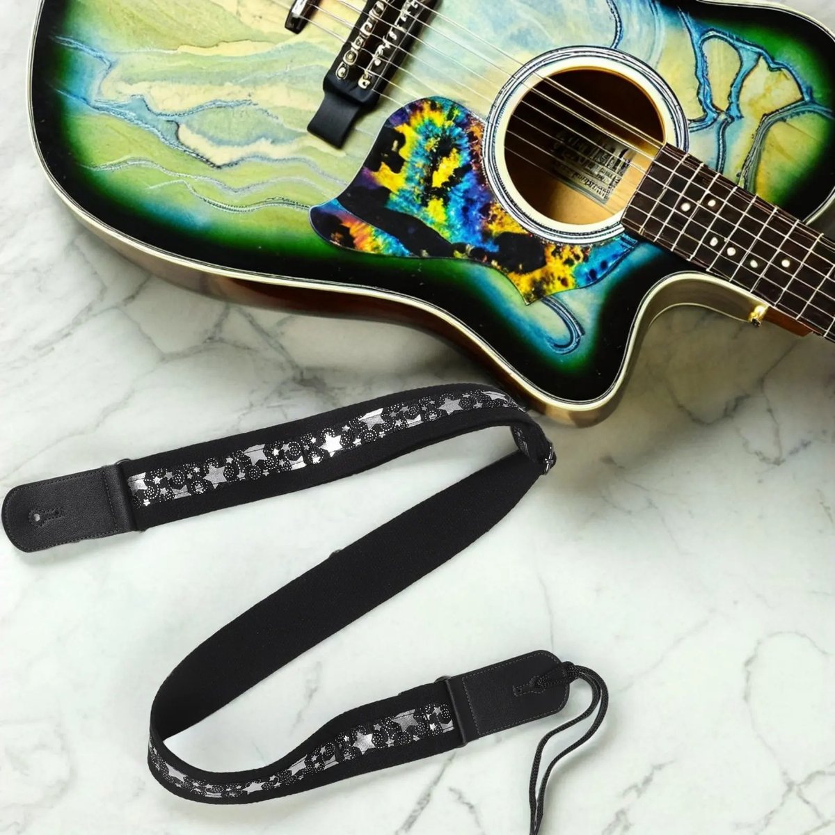 Sangle guitare Silver Night noire à étoiles argentées avec lacet, posée à côté d'une guitare acoustique