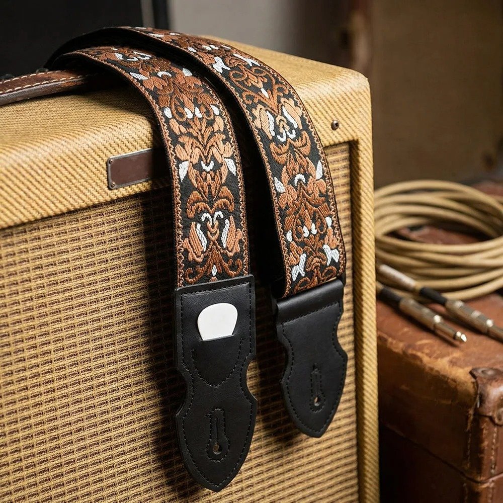 Sangle guitare vintage Baroque Bourbon à motif ornemental cuivré et blanc sur fond noir, posée sur un ampli vintage