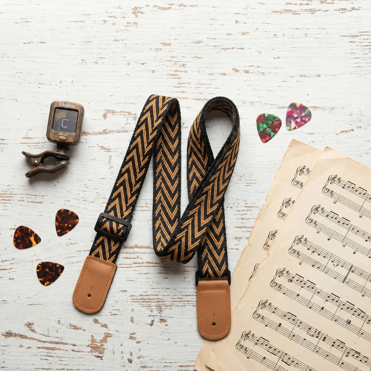 Sangle ukulélé Golden Chevron tissée à chevrons noirs et dorés avec embouts camel, posée sur une table en bois blanc